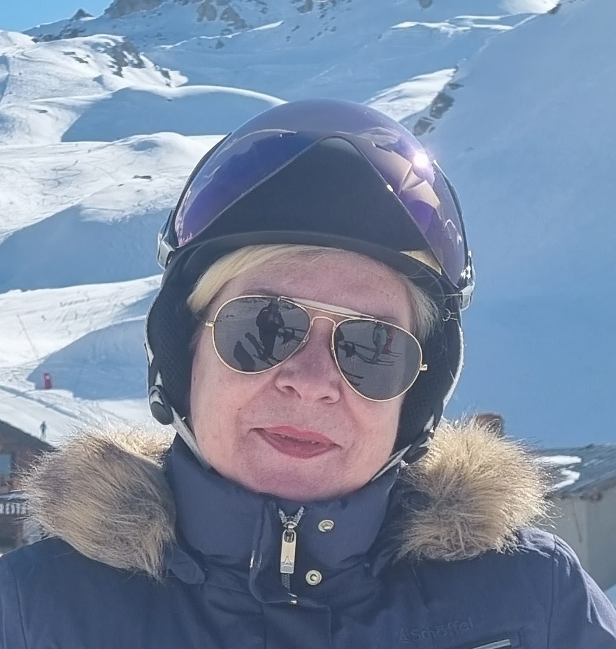 Frau mit Skihelm und Sonnenbrille vor verschneiter Berglandschaft